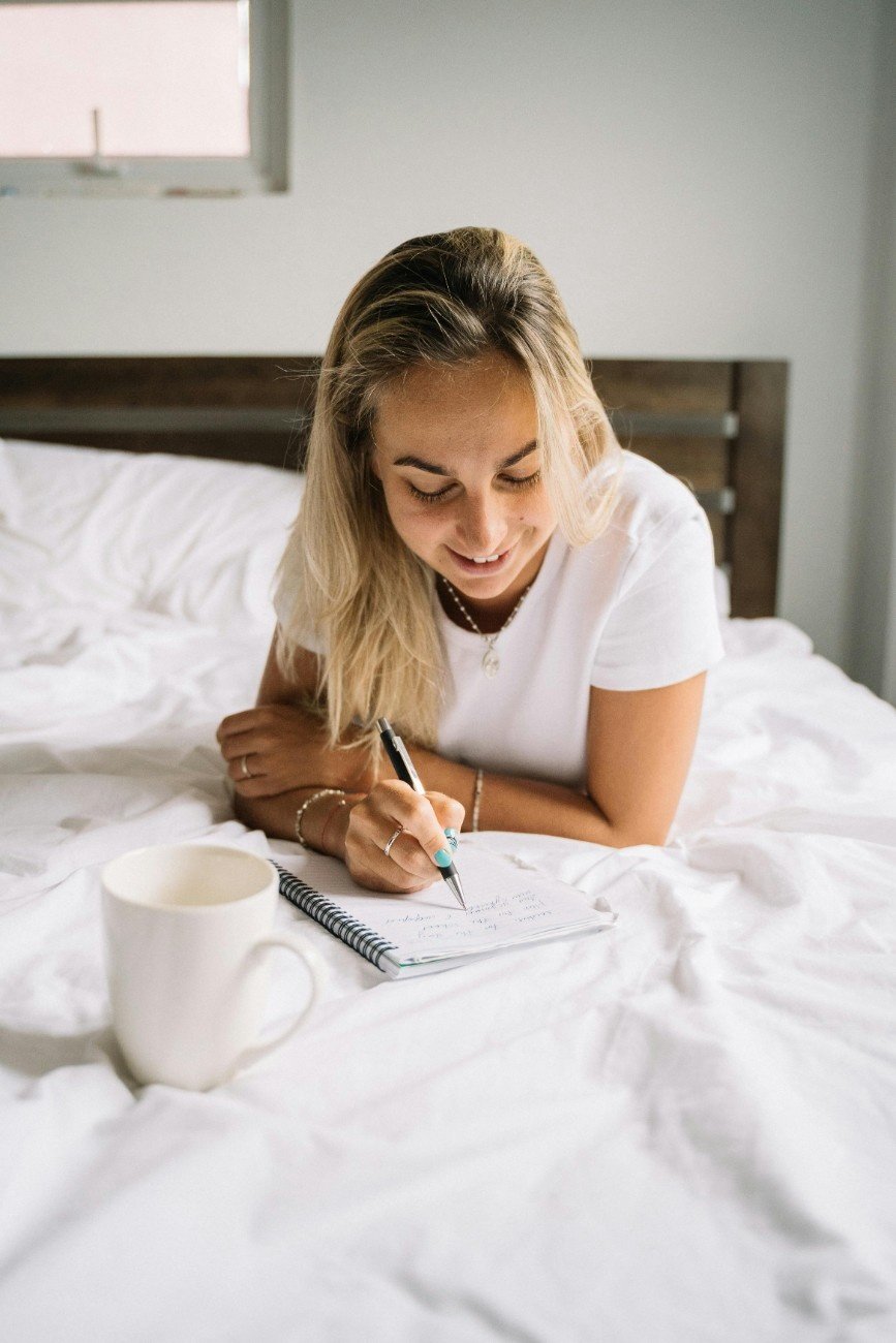 Woman journaling in sunlight with a calm, content smile.