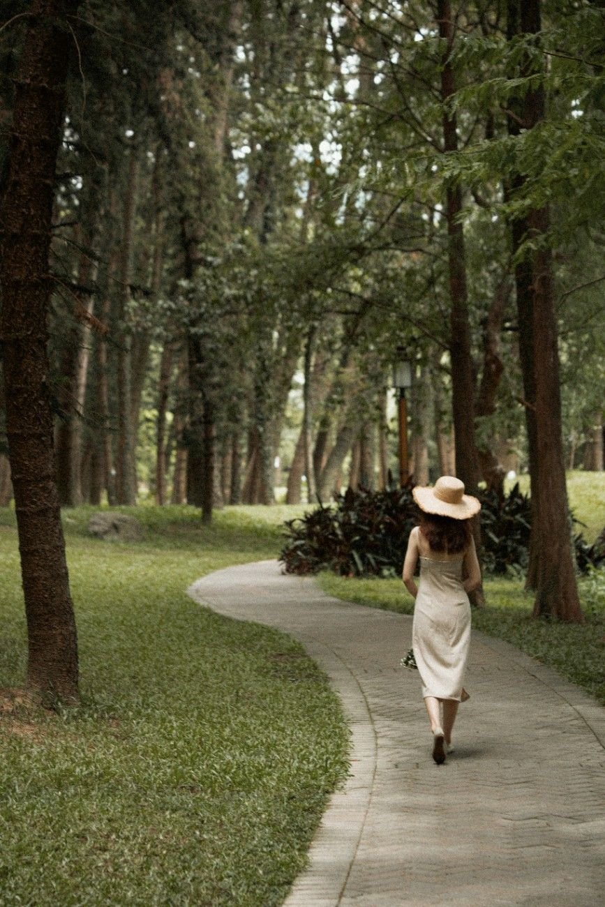 Woman walking alone in sunlight through a quiet park.