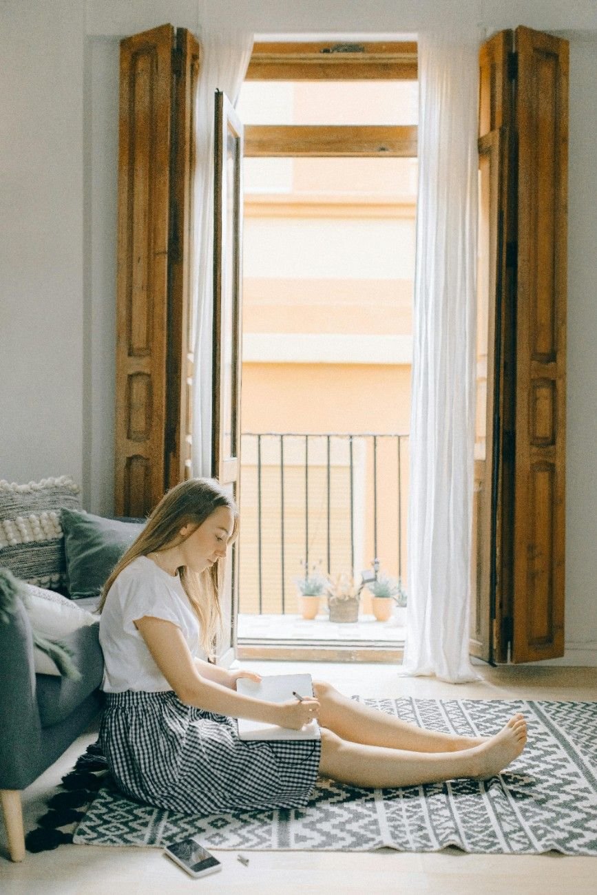 Woman sitting near a window in quiet reflection, soft daylight.