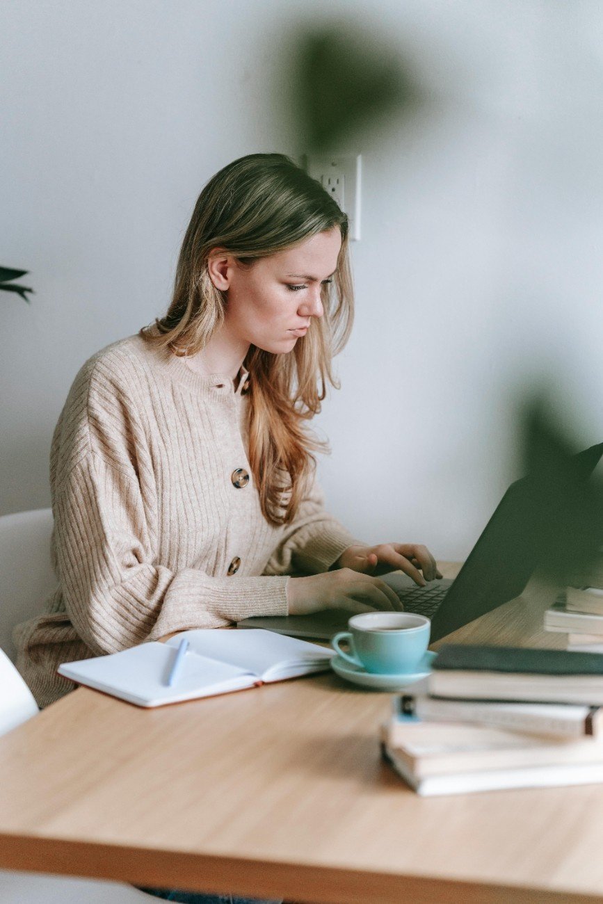 Woman writing in a notebook at a cozy desk with coffee and candle.