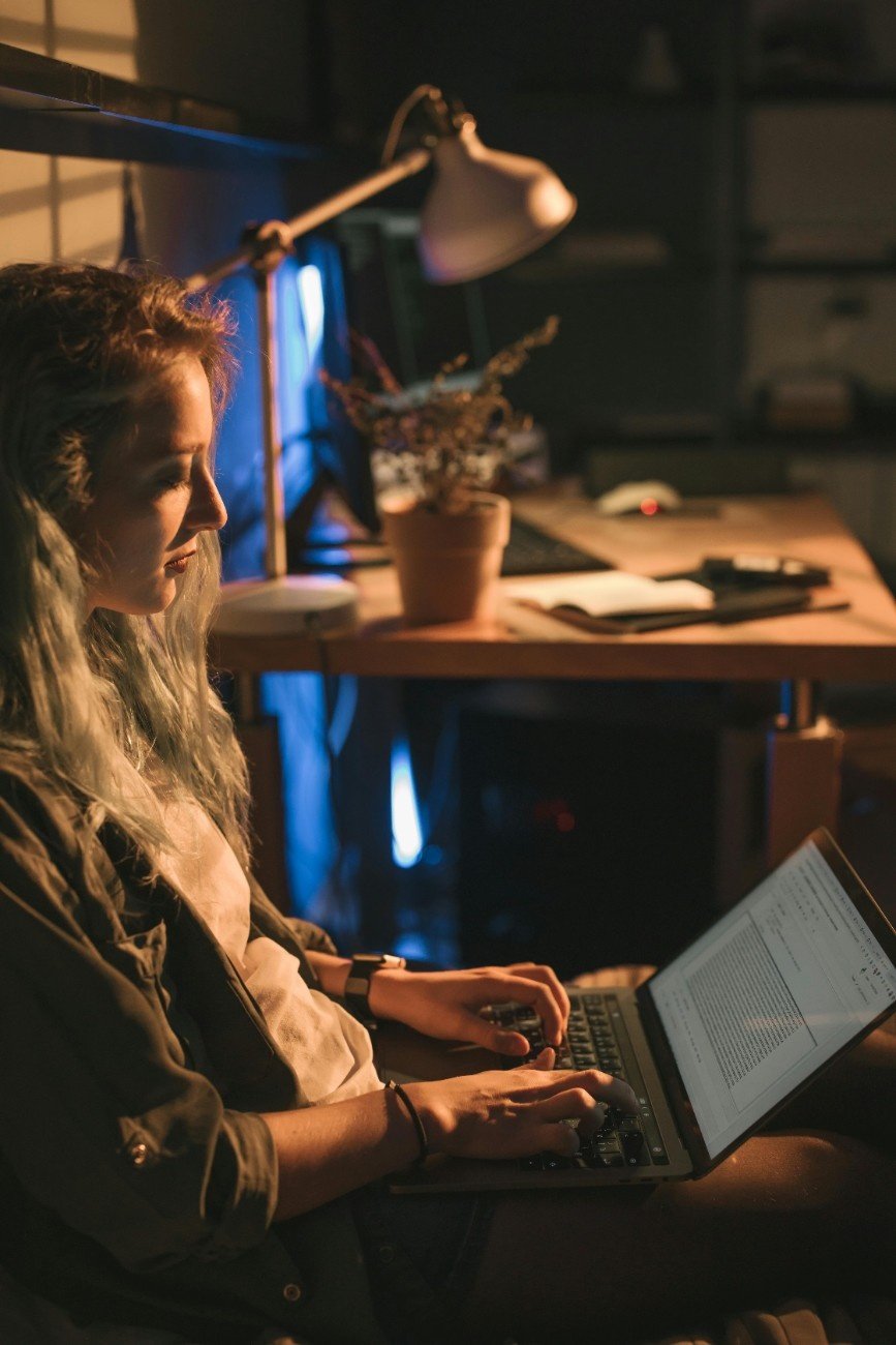 Young woman working on a laptop at night with coffee beside her, balancing a day job and side project.